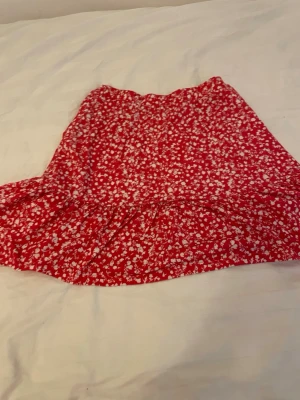 Röd blommig volangkjol - Söt röd kortkjol med vitt blommönster och volang nertill. Perfekt för dig som gillar färg och mönster. Kjolen har en avslappnad passform och är lätt att matcha med en enkel topp.