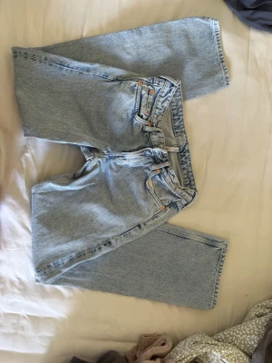 Ljusblå straight leg arrow jeans - Säljer ett par ljusblå arrow jeans med rak passform och låg midja. Jeansen har fem fickor, knappgylf och en läderpatch bak i midjan. Perfekta för en avslappnad och trendig look. Har små fläckar lite här i där men de är inte jättesynliga!