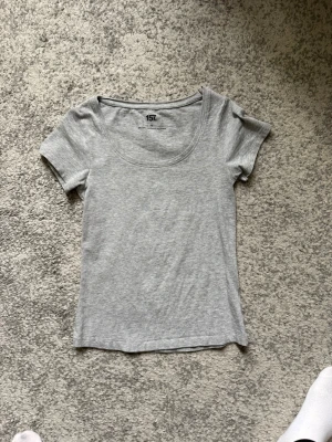 Grå basic topp från 157 - En enkel och stilren grå topp från 157 med rund halsringning och korta ärmar. Tillverkad i mjuk bomull som känns skön mot huden. Perfekt att matcha med jeans eller kjol för en clean look.