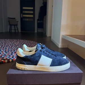 Valentino Garavani sneakers i mocka - Snygga sneakers från Valentino Garavani i mörkblå mocka med vita detaljer och platta nitar på sulan. Skorna är i nyskick med alla nitar kvar, box tillkommer. Skorna är storlek 41 men sitter mer som 42. Bilderna är lite gamla så att det är små slitage längst bak på sulan men inget som märks. Bara att höra av sig vid intresse eller frågor