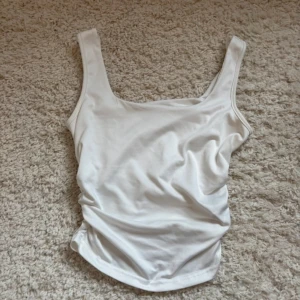 Vit ärmlös linnetopp - Snygg vit linnetopp med breda axelband och rundad halsringning. Toppen är enkel och stilren, perfekt att matcha med olika outfits. Tillverkad i mjukt material som känns skönt mot huden.