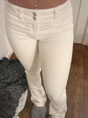 Vita low waist jeans med raka ben - Säljer ett par vita low waist jeans med raka ben och dubbla silverknappar i midjan. Jeansen har bälteshällor och är tillverkade i ett stretchigt denimtyg som sitter snyggt på kroppen. Storlek 170💖