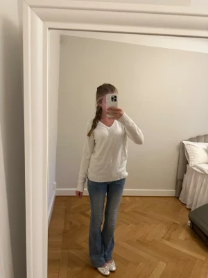 Vit stickad tröja med v-ringning - Klassisk vit stickad tröja med v-ringning och ribbade muddar vid ärmslut och nederkant. Tröjan har en avslappnad passform och är perfekt att matcha med jeans. Materialet ser mjukt och bekvämt ut, perfekt för kyligare dagar.