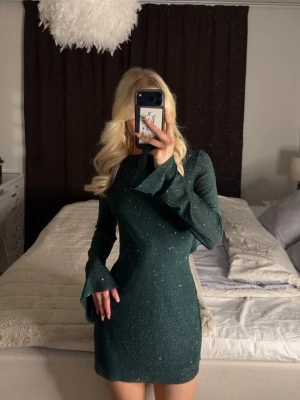 Glittrig grön minidress med öppen rygg - Nyskick då jag burit den endast en gång, passar perfekt till fest, jul men även nyår. Galet vacker klänning jag dragit mig för att sälja, men jag hinner inte använda den som den förtjänar, storleken är S och sitter bra och bekvämt. Den är luftig i materialet och elegant i rörelse