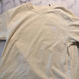 Beige vit t shirt  Ami Paris - Säljer en stilren beige tshirt från Ami. Helt ny med tags, säljer pga ingen användning samt rensar garderob.      Modellen har ett tjockt material perfekt för sommarkvällar.  Storlek S/M.            Ny pris: 1099-1300.   Mitt pris: 549 eftersom jag vill rensa snabbt garderoben