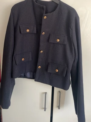 Mörkblå kavaj med guldknappar - Stilren mörkblå kavaj med fyra framfickor och dekorativa guldknappar. Jackan har rak passform, rund halsringning och är helfodrad. Perfekt för en trendig och klassisk look.