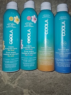 COOLA solskyddsspray SPF 30/50 - Fyra flaskor COOLA solskyddsspray i olika dofter och SPF-nivåer. Innehåller varianter som Pina Colada, Guava Mango, Tropical Coconut och en parfymfri version. Flaskorna är turkosa med vita lock och har blommiga detaljer. Sprayen är transparent och ger högt skydd.
