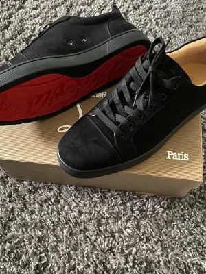 Svarta Loubs - Snygga svarta sneakers från Christian Louboutin med klassisk röd sula och svarta skosnören. Ovandelen är i mocka och detaljer i läder. Perfekta för dig som vill ha en clean och exklusiv look med en ikonisk touch. Oanvända då den jag köpt av skrivit att skrona var strlk 46 istället för 44. Har endast provat dem.