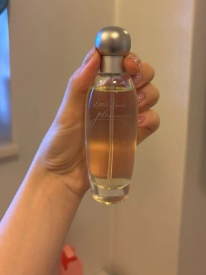 Estée Lauder Pleasures EdP 50ml - Estée Lauder Pleasures Eau de Parfum i 50 ml flaska. Parfymen kommer i en elegant, genomskinlig glasflaska med rundad silverfärgad kork och har en ljusrosa förpackning. Doften är klassisk och feminin, perfekt för dig som gillar fräscha och blommiga toner.