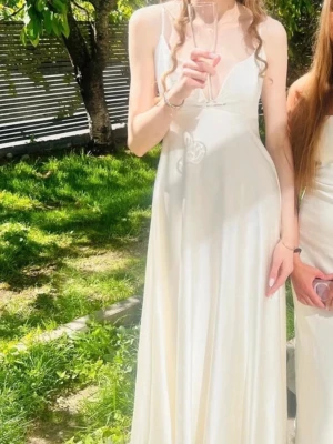 Balklänning studenten prom dress - Elegant vit långklänning med smala axelband och v-ringning. Klänningen har en mjuk, glansig yta som ger ett exklusivt intryck och ett flytande fall. Perfekt för sommarens speciella tillfällen.