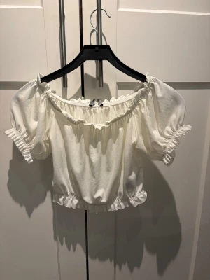 Vit offshoulder topp  - Söt vit offshoulder topp från Gina Tricot med puffärmar och volangdetaljer vid halsringning, ärmslut och nederkant. Jättefin till sommaren☀️🩷
