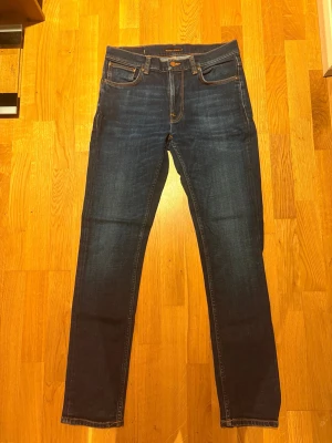 Mörkblå slim fit jeans från Nudie 32L 32W, Lean Dean - Snygga mörkblå slim fit jeans från Nudie Jeans. Jeansen har en rak passform och är tillverkade i denim för extra komfort. Perfekta för en avslappnad och stilren look. Modell är lean Dean 32L 32W