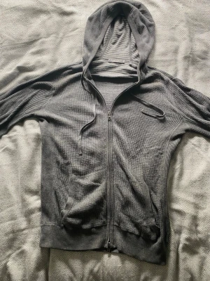 Grå zip hoodie från Vince - Säljer en grå hoodie från Vince i storlek S. Hoodien har dragkedja framtill, två fickor och justerbar huva med snören. Materialet är mjukt och har en ribbad, strukturerad yta som ger en avslappnad look. Perfekt för chill dagar eller när du vill vara bekväm.