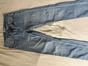 Ljusblå raka jeans - Säljer ett par ljusblå jeans med rak passform och klassisk femficksdesign. Jeansen har normal midja och stängs med dragkedja och knapp. Materialet är denim i bomull och de har en avslappnad vintagekänsla.