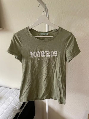Grön t-shirt från Morris Lady - Snygg grön t-shirt från Morris Lady med vit broderad logga framtill. Klassisk rund halsringning och korta ärmar. Perfekt till jeans eller kjol för en avslappnad och trendig look.