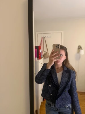 Mörkblå tweedkavaj från Zara - Snygg mörkblå tweedkavaj från Zara med dubbelknäppning och dekorativa silverknappar. Kavajen har markerade axlar, kortare passform och fina detaljer längs kragen. Perfekt för en trendig och stilren look.