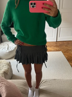 Grå kortkjol med snörning och ränder - Säljer en grå kortkjol med tunna vita ränder och snörning i sidorna. Kjolen har plisserad nederkant och en cool, ungdomlig vibe. Perfekt för dig som gillar trendiga detaljer och vill sticka ut lite extra.