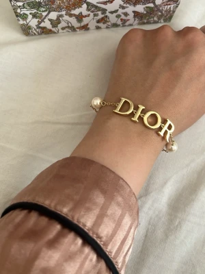 Armband med pärlor och guld - Snyggt armband i guldfärgad metall 18k guldpläterad med stora bokstäver. Armbandet har två vita pärlor på sidorna som ger en lyxig känsla. Perfekt accessoar för dig som vill sticka ut och visa din stil. Priset är utan paketering och med paketering blir det 200kr mer. Kolla min profil för att se hur paketeringen kan se ut.