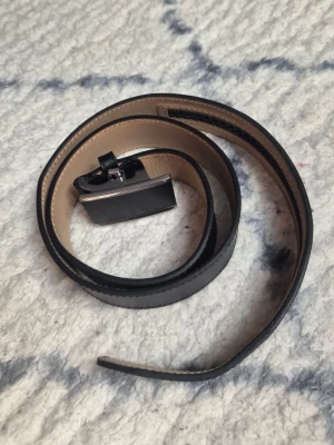 Svart skärp från Dressmann i skinn - Snyggt svart bälte från Dressmann i äkta skinn med stilren metallspänne. Bältet har en klassisk design och passar perfekt till jeans eller kostymbyxor. Insidan är beige och utsidan är svart, vilket ger en clean kontrast.