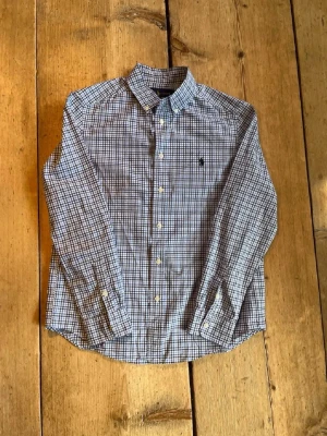 Blårutig skjorta från Ralph Lauren - Klassisk blårutig skjorta från Ralph Lauren med button-down krage och broderad logga på bröstet. Skjortan har långa ärmar, knäppning framtill och är tillverkad i bomull med stretch för extra komfort.