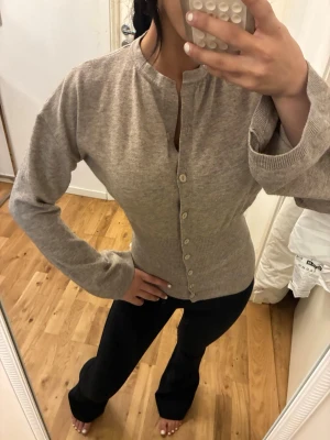 Beige ribbad kofta med knappar - Säljer en beige ribbad kofta med rund halsringning och knäppning framtill. Koftan har långa ärmar och en smal, figurnära passform. Perfekt att slänga över en topp eller bära stängd för en clean look.