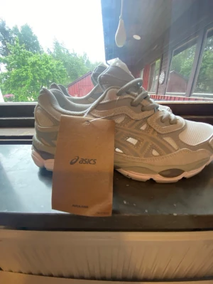 Beige sneakers från Asics - Snygga sneakers från Asics i beige och vitt med meshpaneler och detaljer i syntet. Skorna har en chunky sula och klassisk snörning. Perfekta för dig som gillar sportig stil och vill ha bekväma skor till vardags.