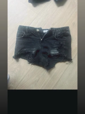 Svarta slitna jeansshorts från ZARA - Säljer ett par svarta jeansshorts från ZARA med råa, slitna kanter och flera revor för en edgy look. Shortsen har klassisk femficksdesign, knapp och dragkedja framtill samt låg midja. Perfekta för sommaren och festivaler.