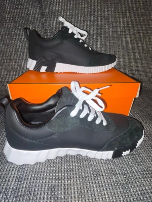 Svarta sneakers med vit sula - Snygga svarta sneakers med vit, räfflad sula och vita skosnören. Ovandelen är i en mix av mocka och textil, med detaljer i svart och mörkgrått. Skorna har en modern, chunky look och dragflik bak för enkel påtagning.