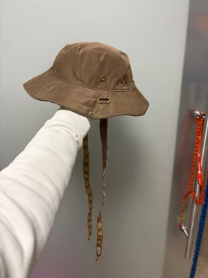  Gucci hat - Säljer en beige bucket hat från Gucci med vändbar design. Ena sidan är enfärgad med diskret GG-logga och guldfärgade detaljer, andra sidan har klassiskt GG-mönster. Hatten har långa knytband med logga och är tillverkad i ett lätt, slitstarkt material.