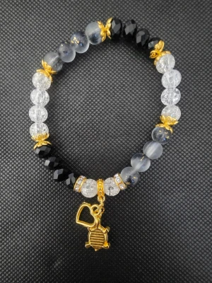 Handgjort armband med guldfärgad sköldpaddshänge - Handgjort elastiskt armband med svarta, genomskinliga och gråmelerade pärlor. Dekorerat med guldfärgade detaljer och ett hänge i form av en sköldpadda samt ett hjärta. Perfekt accessoar för dig som gillar unika smycken med djurmotiv.