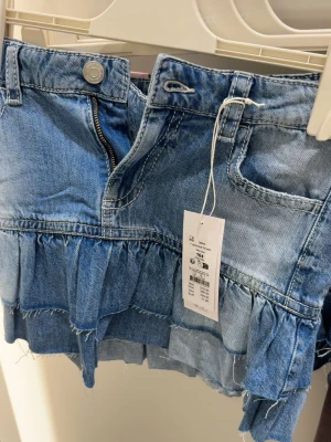 Blå trendig volang kjol - Säljer en kort jeanskjol med volangdetaljer från Gina tricot. Helt ny, oanvänd med lappen kvar. Säljs pågrund av att den är för liten.💞