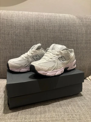 Vita New Balance sneakers  - Snygga vita sneakers från New Balance med mesh- och syntetdetaljer. Skorna har en chunky sula i vitt och svart, samt det klassiska N-logot på sidan. Perfekta för dig som gillar sportig och trendig stil.