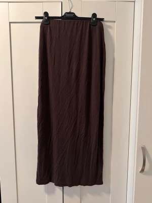Brun långkjol i bomull - En enkel och stilren brun långkjol i mjukt bomullstyg. Kjolen har rak passform och är perfekt för dig som gillar minimalistisk stil. Inga synliga detaljer eller mönster, bara en clean look som funkar till det mesta.