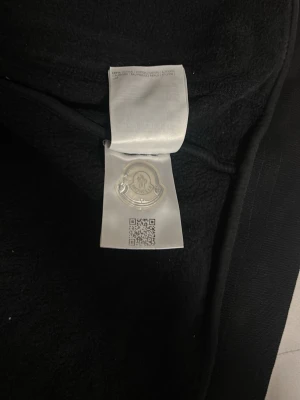Svart Moncler fleecejacka - Snygg svart fleecejacka från Moncler med ribbade muddar. Jackan har en klassisk design och är tillverkad i mjuk fleece som håller dig varm. Perfekt för dig som vill ha en stilren och bekväm jacka med exklusiv känsla. Den är äkta den är storlek L/M
