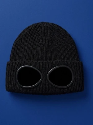 Svart C.P. Company goggle-mössa - Säljer en svart stickad mössa från C.P. Company med de ikoniska inbyggda goggles framtill. Mössan är ribbstickad och har en cool, urban vibe som sticker ut. Perfekt accessoar för dig som vill ha något unikt och trendigt.