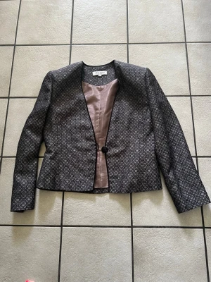 Mönstrad svart kavaj från Jane Lorisa storlek L - Snygg svart kavaj med diskret geometriskt mönster i grått. Kavajen har en knapp framtill, rak passform och ljusrosa foder. Perfekt för att lyfta din outfit med en unik touch.