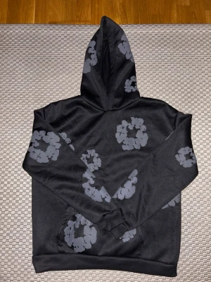 Svart Denim tear  hoodie - Säljer en svart hoodie med huva och unikt grått mönster i form av cirklar över hela tröjan. Hoodien har en klassisk passform och magficka framtill. Materialet känns mjukt och bekvämt, perfekt för en avslappnad stil.