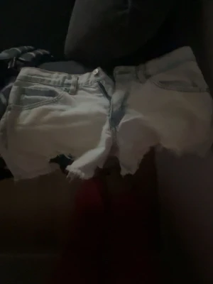 Ljusblå jeansshorts med fransig kant - Säljer ett par ljusblå jeansshorts med rå, fransig kant och slitna detaljer. Klassisk femficksmodell med knapp och dragkedja framtill. Perfekta för sommaren och ger en avslappnad vibe.