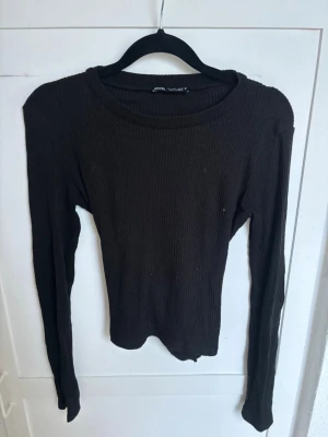 Svart ribbad långärmad topp - Säljer en svart ribbad långärmad topp från Gina Tricot. Toppen har en tight passform och en snygg knytning i ryggen som ger en unik look. Perfekt att styla med jeans eller kjol för en trendig outfit.