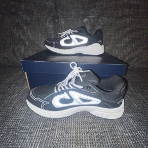 Svarta CD sneakers med vit sula - Snygga svarta sneakers från CD med vit tjock sula och reflekterande detaljer. Skorna har en sportig design med vita snören och stora CD-loggor på sidan. Ovandelen är i mesh och syntetmaterial för en modern look.