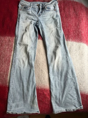 Ljusblå bootcut size s jeans - Säljer ett par ljusblå bootcut jeans med klassisk femficksdesign och låg midja. Jeansen har utsvängda ben och är tillverkade i mjuk denim. Perfekta för en avslappnad och trendig look.