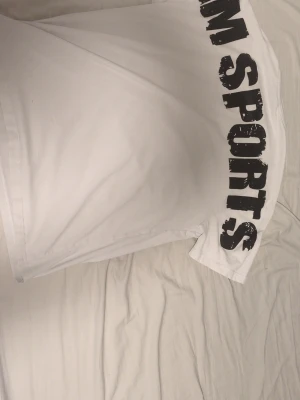 Vit t-shirt från MM Sports baggy - Säljer en vit t-shirt från MM Sports med svart tryck på bröstet och längs sidan. Klassisk rund hals och korta ärmar. Perfekt för dig som gillar enkel och sportig stil. Materialet känns mjukt och bekvämt. 