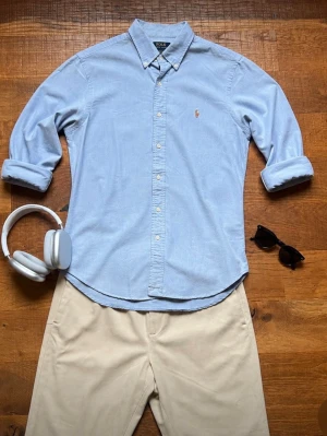 Ralph Lauren Skjorta Herr Small Slim Fit Ljusblå - Klassisk Polo Ralph Lauren Oxford-skjorta i ljusblå färg med broderad logga på bröstet. En av Ralph Laurens mest eftertraktade modeller som passar perfekt till chinos, jeans eller shorts. Tidlös preppy- och old money-stil som fungerar året runt.                                    Kommer från ett rökfritt hem.                           Snabb leverans 📦                                   Bundledeals finns    
