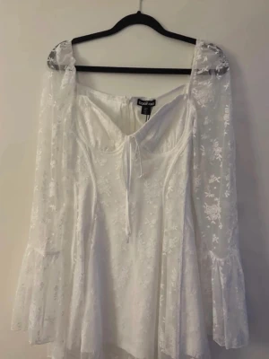 Vit blommig klänning från Boohoo - Romantisk vit klänning från Boohoo med blommigt spetsmönster, långa transparenta ärmar och söt snörning framtill. Helt ny testad bara en gång!