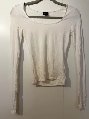 Vit långärmad topp från Gina Tricot - En enkel och stilren vit långärmad topp från Gina Tricot. Modellen har rund halsringning och är gjord i mjuk bomull som är skön att bära. Perfekt att matcha med jeans eller kjol för en clean look. Observera att den inte är smutsig längst ner utan bilden är tagen i dåligt ljus! ❣️😊