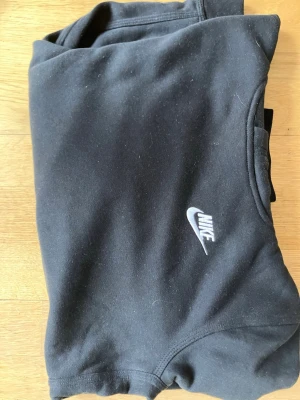 Svarta mjukisbyxor från Nike - Säljer ett par svarta mjukisbyxor från Nike med klassisk vit logga på benet. Byxorna har resår i midjan och är gjorda i mjukt bomullsmaterial som är riktigt skönt att ha på sig. Perfekta för chill eller träning. Stl 147-158