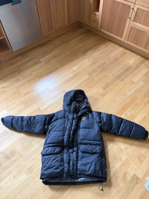 Svart dunjacka med huva från Fjällräven - Säljer min Fjällräven-jacka då den tyvärr är för stor för mig. Märkt S men är väldigt oversized och passar mer som en L/XL beroende på hur man vill att den ska sitta. Såå varm och skön på vintern och sjukt snygg på. Har lite slitage/skavanker vid dragkedjan/knäppningen men inget som påverkar användningen. Annars är den i fint skick och har massor av liv kvar. Perfekt om du gillar en större passform eller vill kunna ha tjocktröja under. 🫶💕