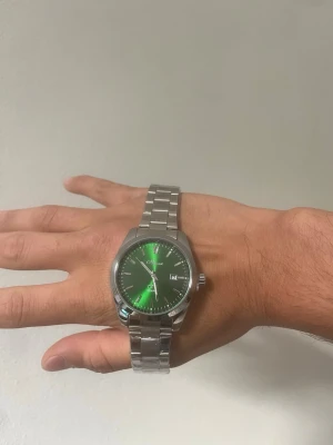 Grön klocka + plus Klockarmbandsverktyg - Snygg klocka  grön urtavla och datumvisning. Klockan har en klassisk rund form och en länk i silverfärgat stål som ger en clean och modern look. Perfekt accessoar för dig som vill sticka ut lite extra.
