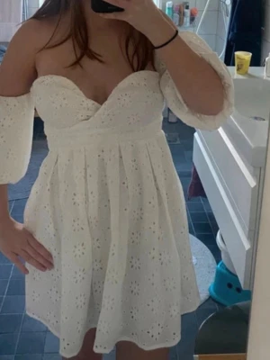Vit offshoulder klänning med spets - Supersöt vit kortklänning med offshoulder och puffiga ärmar. Klänningen har broderade spetsdetaljer i blommigt mönster och omlott över bysten. Perfekt för sommarens alla tillfällen!