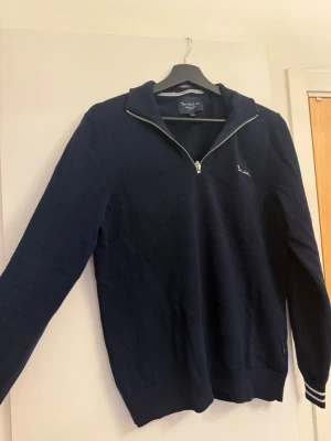 Mörkblå halvzip-tröja från Bondelid - Mörkblå stickad tröja från Bondelid med halv dragkedja och liten broderad logga på bröstet. Tröjan har ribbade muddar vid ärmslut och nederkant samt en klassisk krage. Perfekt för en stilren och avslappnad look. Varan är i super skick, inga skador osv.